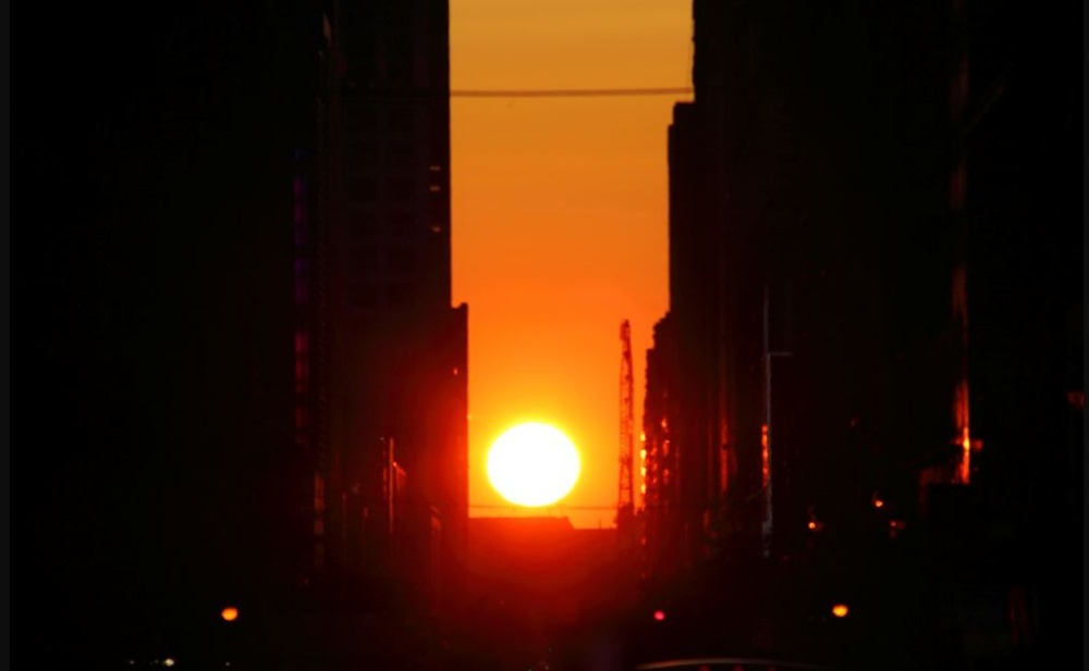 The Manhattanhenge sunset with the sun rays streaming through tall buildings.