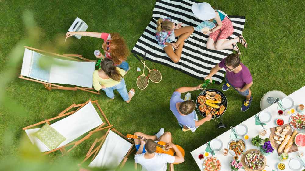 High angle view of group of people having backyard barbecue party with grill, guitar, deck chairs and delicious food on the table