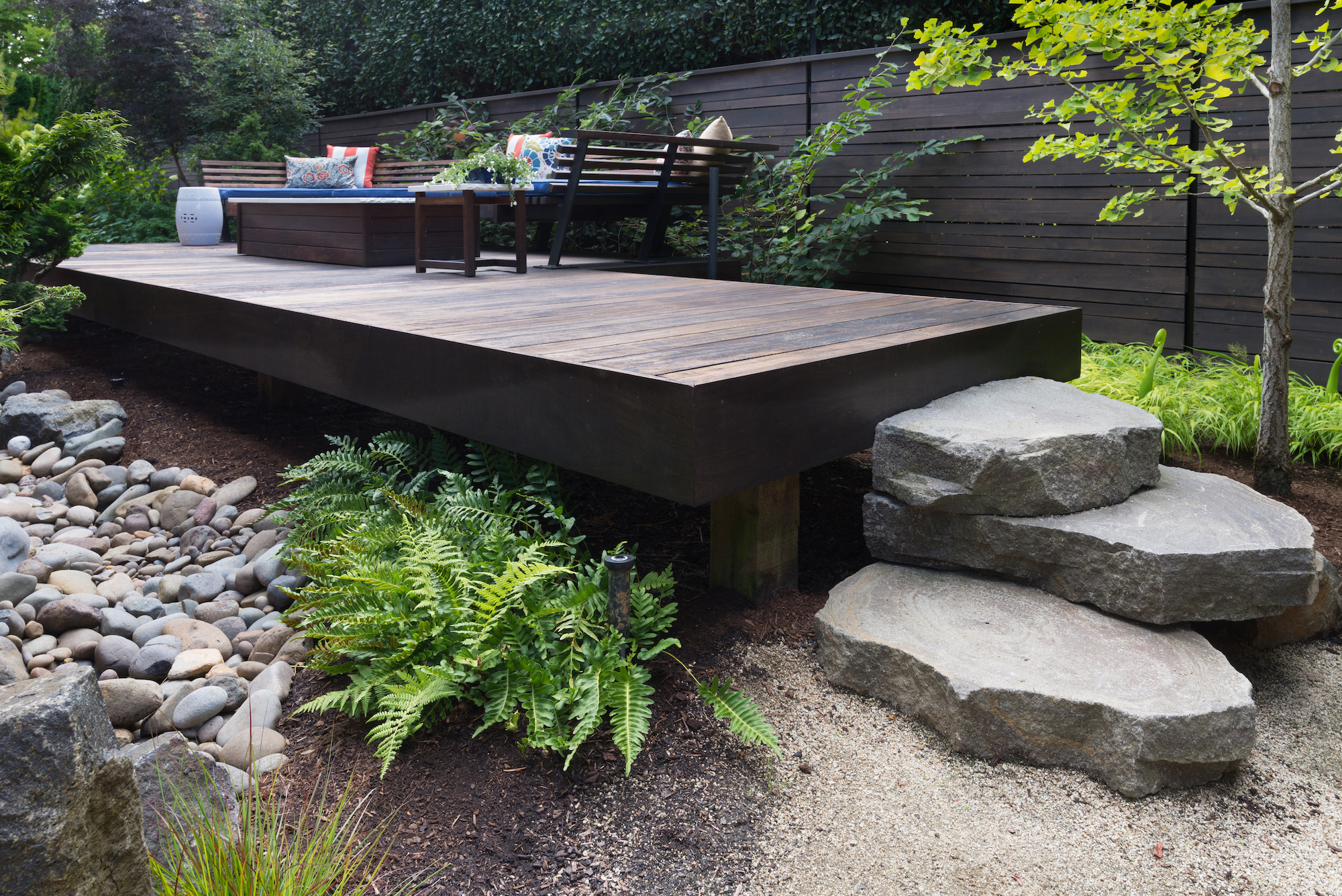 Three massive rocks form steps to a contemporary deck with rocks below. 