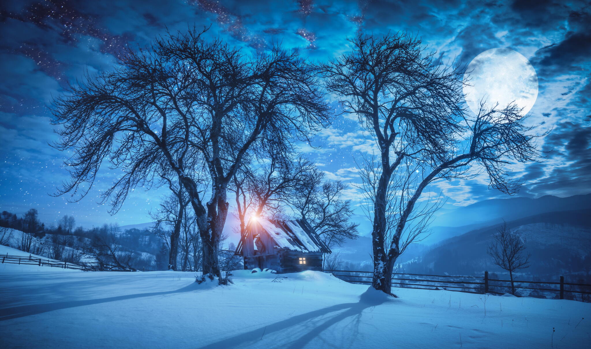 Full Moon rises over a fairy wooden house under the trees on a snowy hill.