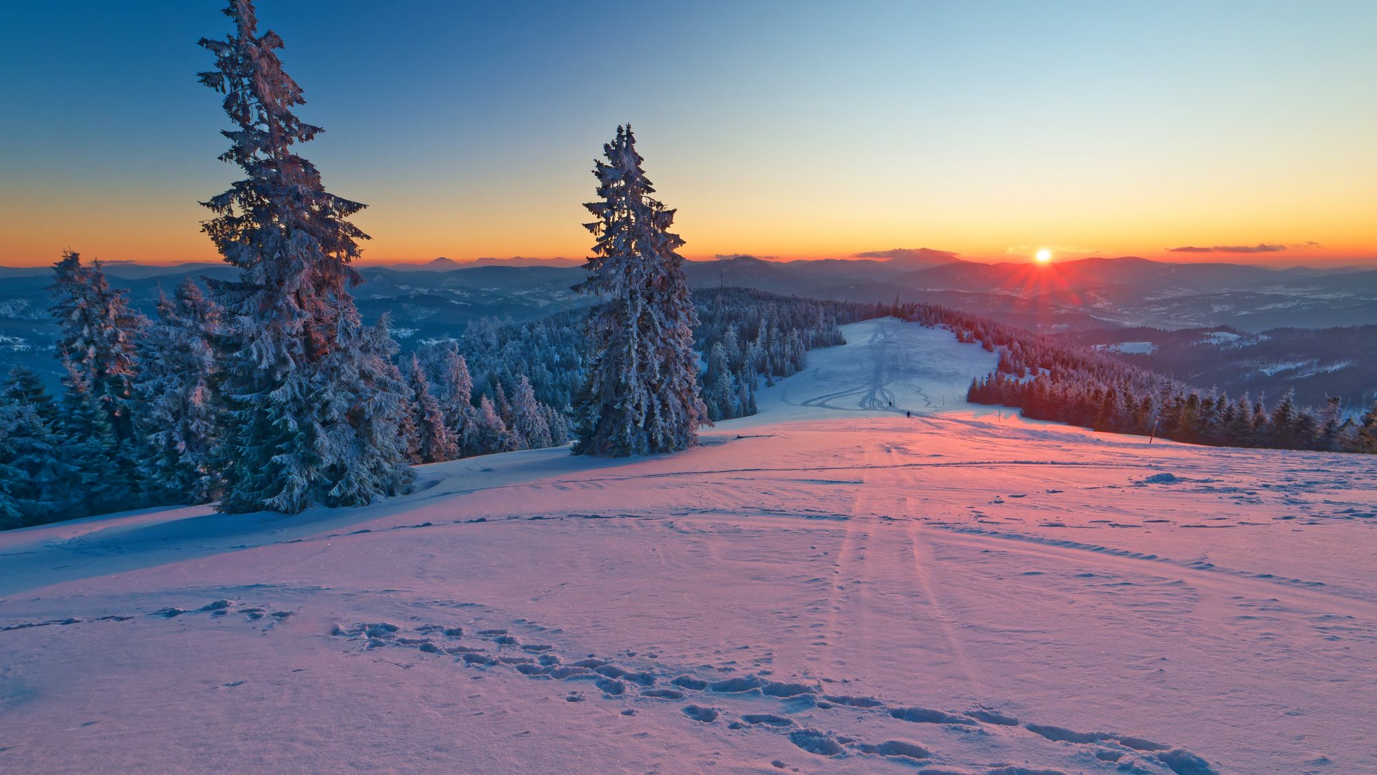 Winter sunset in the Beskid Żywieckie mountains. The place is called Hala Redykalna. The warm colors of the setting sun illuminate the snow and snow-covered trees.​